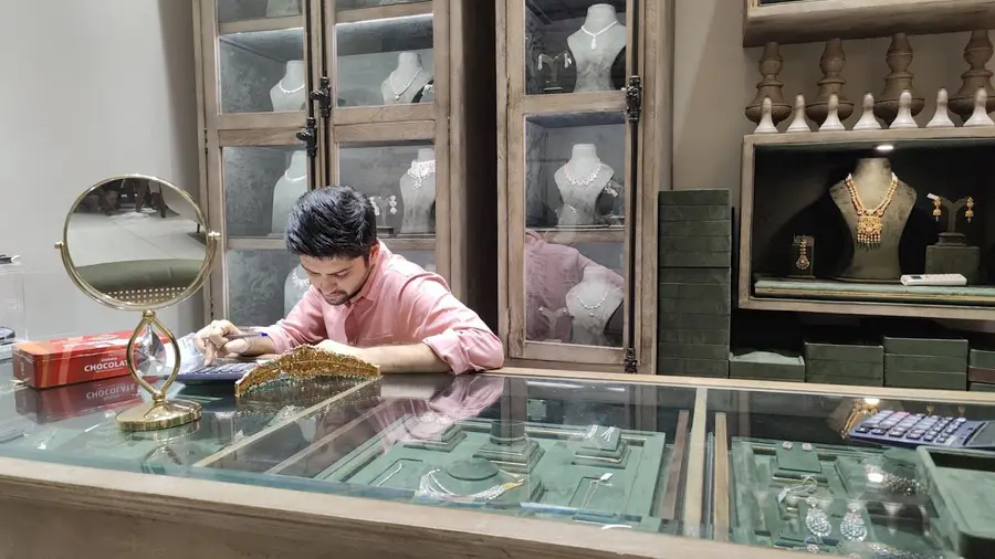 A member of staff laying a piece into a glass display case, a bridal set on green velvet in the case below.