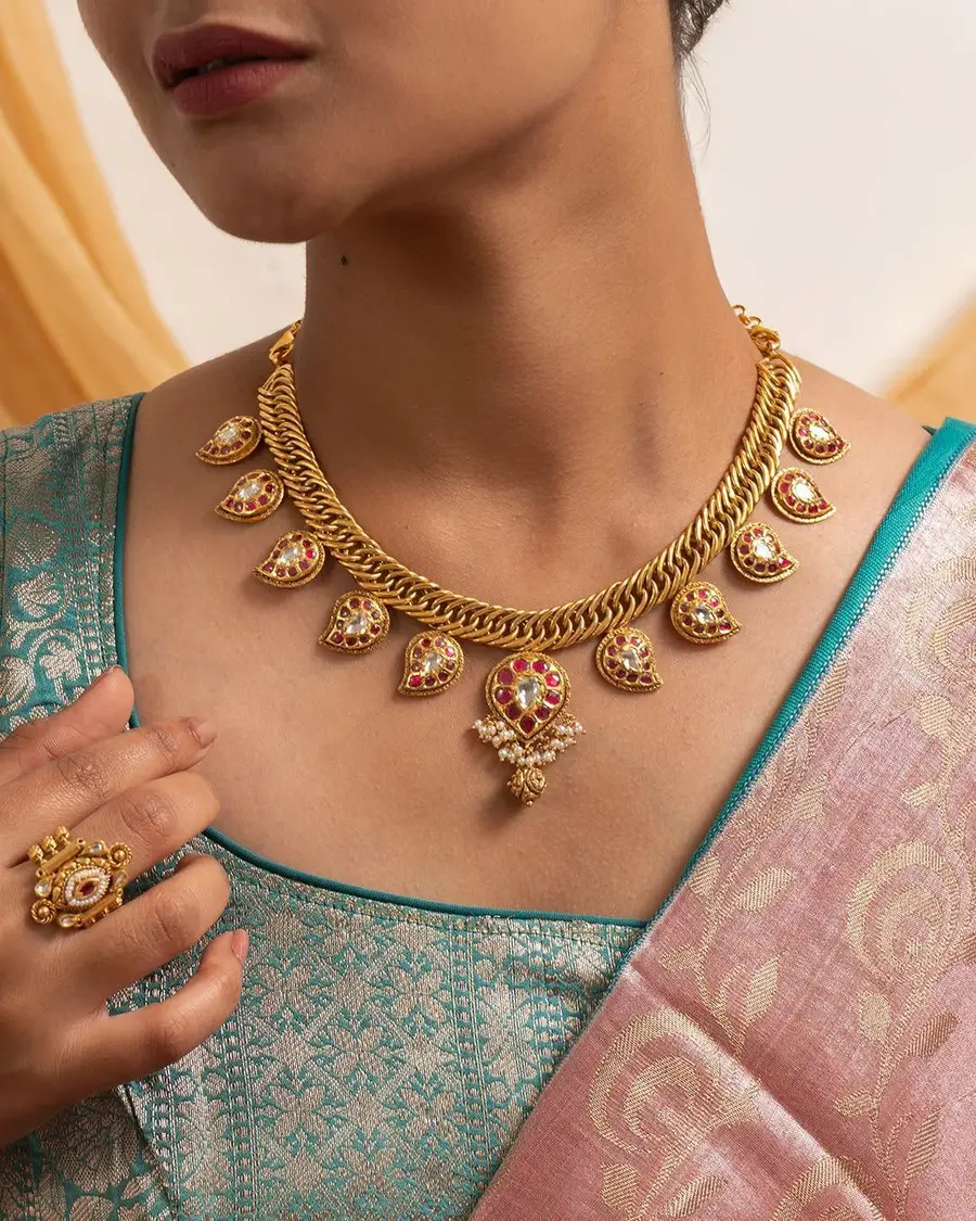 A gold necklace with stone-set drops worn over a teal and gold silk saree, with a matching ring.